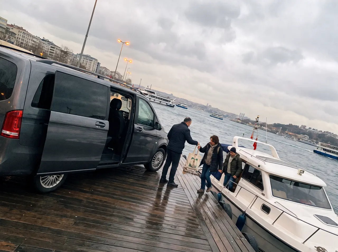 Driver waiting by a car near a Bosphorus pier at dusk